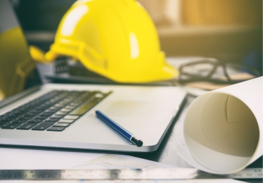 Yellow hard hat next to computer and construction blueprint