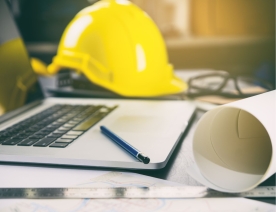 Yellow hard hat next to computer and construction blueprint